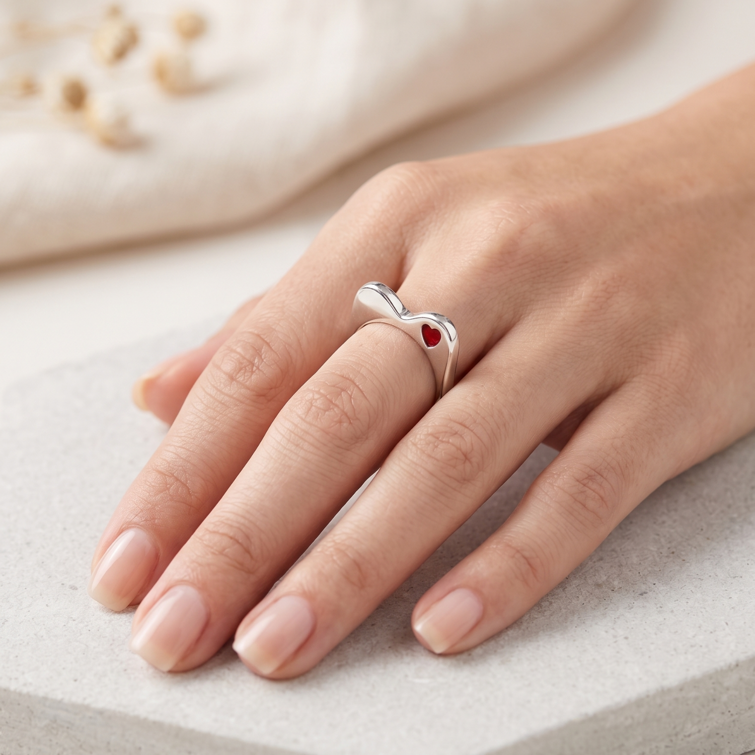 Silver ring with a red heart on a hand against a neutral background